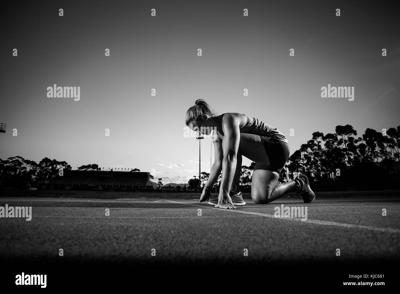 Nahaufnahme Weitwinkelaufnahme eines weiblichen sprinter Athlet fertig, ein Rennen auf einen tartan Rennstrecke mit dramatischen Beleuchtung am späten Nachmittag zu starten Stockfoto