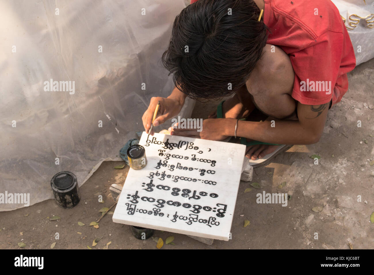 Eine burmesische Lokale schreibt eine alte Inschrift auf einem Block von Marmor mit schwarzer Farbe an einem Buddha carving Workshop in Mandalay. Stockfoto