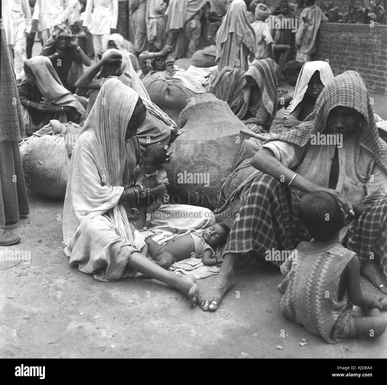 Ein Bild von Flüchtlingen, die sich außerhalb der Kantine Wavell versammelt haben, möglicherweise während oder nach einem größeren Konflikt, die auf den Transport in sicherere Orte oder Lager warten. Stockfoto