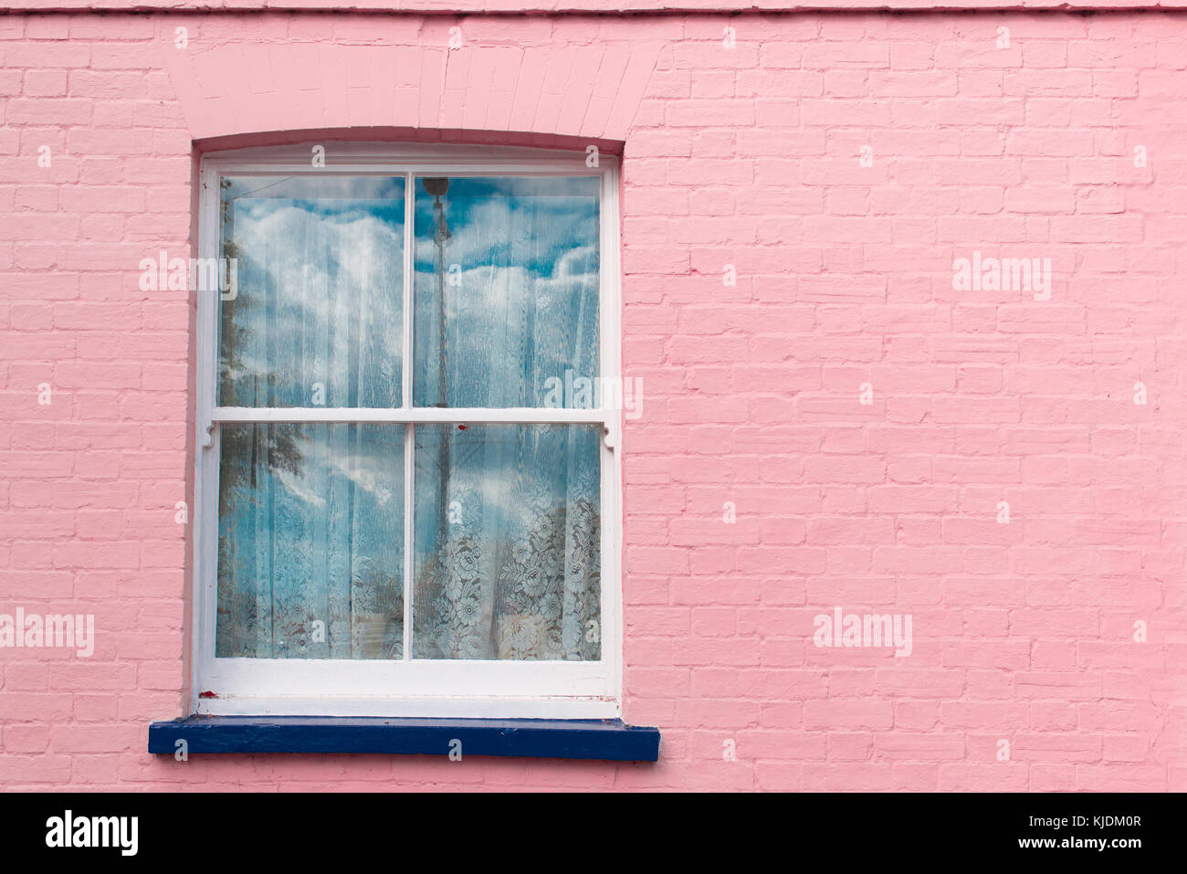 Viktorianisches Fenster mit weißen Holzmöbeln Schärpe, weiße Vorhänge und blauen Balkon auf einem hellen rosa bemalten Wand Stockfoto