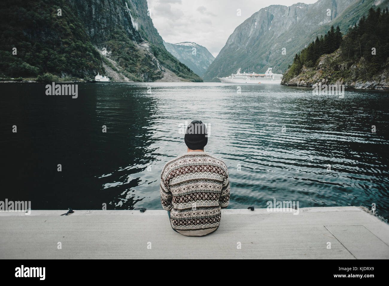 Kaukasische Mann sitzt auf Dock beobachten Kreuzfahrtschiff Stockfoto