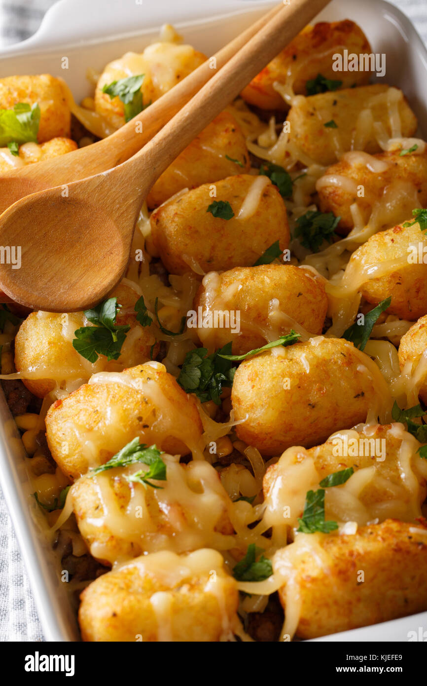 Auflauf von Tater Tots mit Käse und Kräutern aus der Nähe in einer Schüssel Auflaufform auf den Tisch. Vertikale Stockfoto