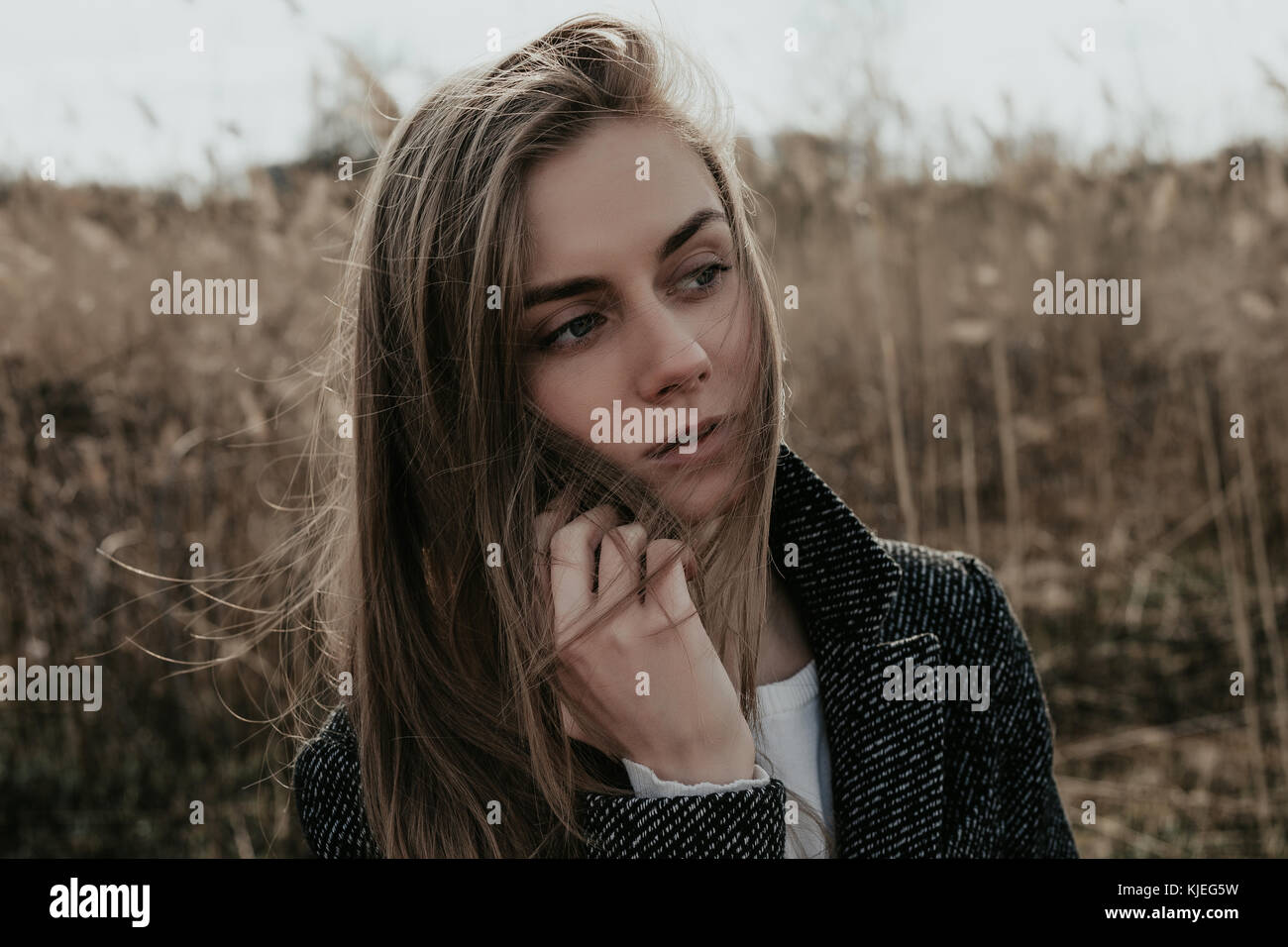 Hübsche Frau mit langen blonden Haaren stehen auf rohrkolben Hintergrund  und Sprechen auf Mobile. Mädchen gekleidet in Mantel. Modell seitlich auf  der Suche. Breite hautnah Stockfotografie - Alamy