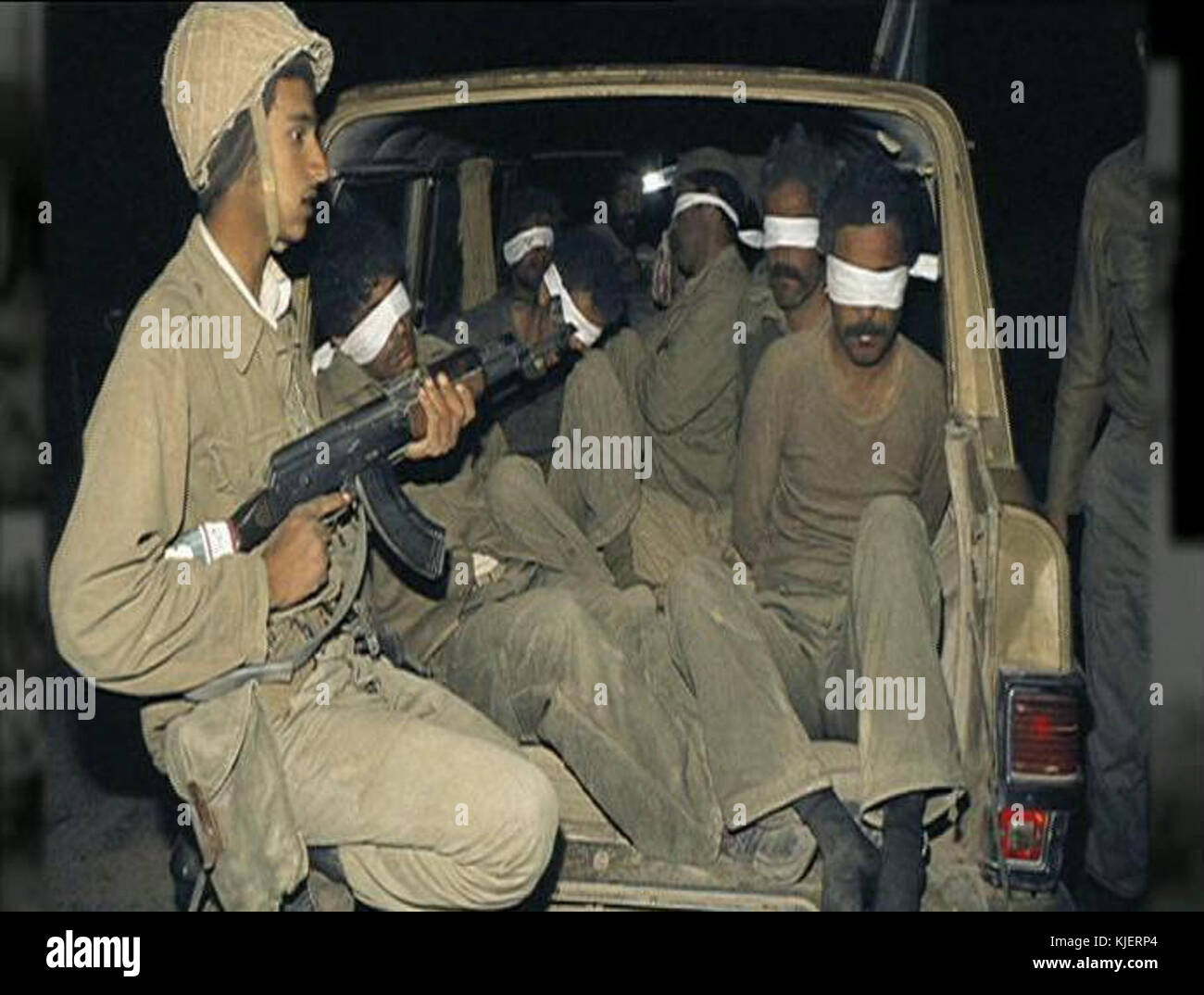 Ein Foto aus einem Konflikt, das einen iranischen Soldaten zeigt, der irakische Gefangene beobachtet, die in einem Pickup sitzen und die Realitäten des Krieges und der Gefangenschaft während des Iran-Irak-Konflikts widerspiegelt. Stockfoto