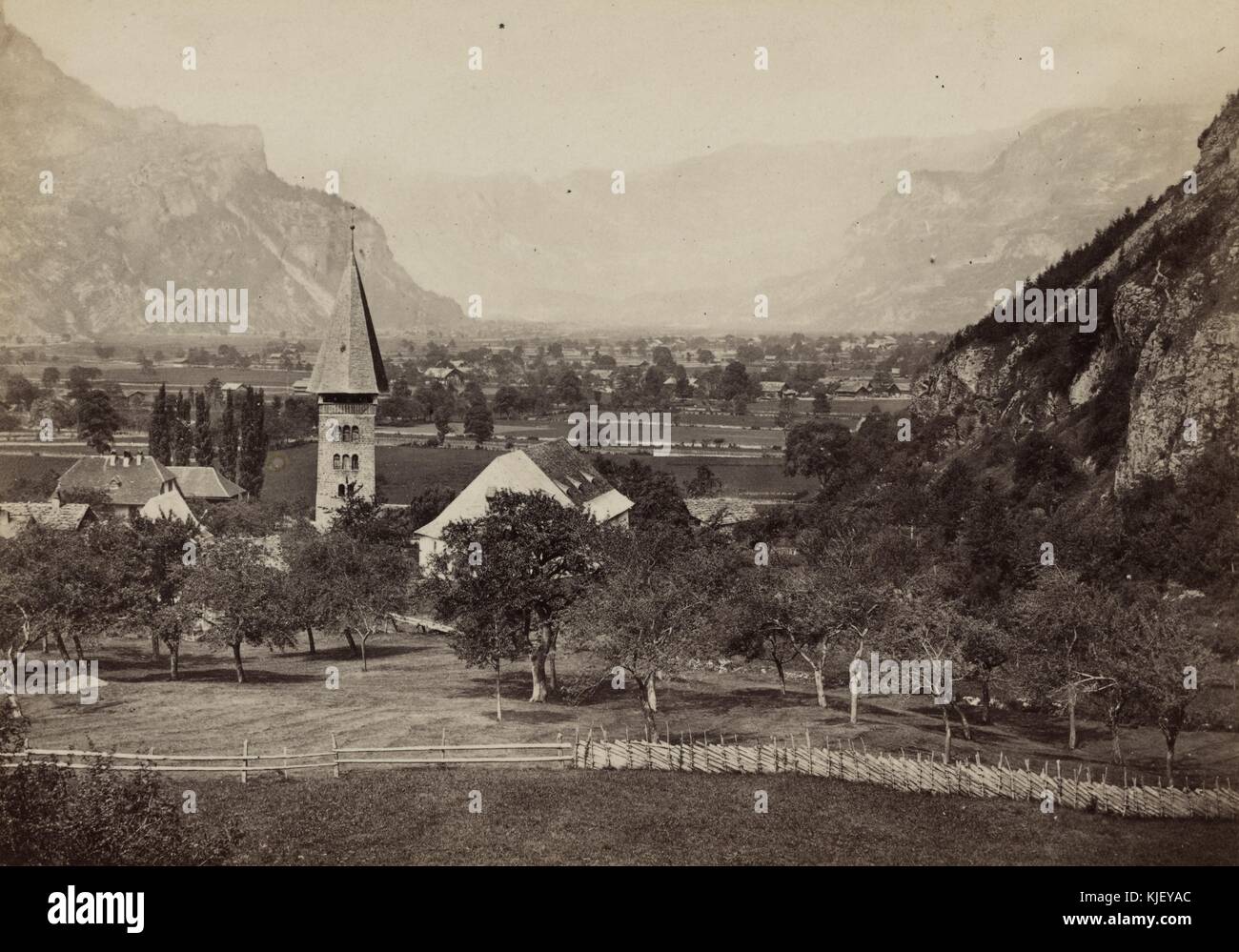 Ein Foto der Stadt Meringen von einer Höhe über der Stadt auf einem Hügel, die Stadt ist in einem Tal, umgeben von hohen Bergen, zu sehen, der Turm einer Kirche im Vordergrund zusammen mit mehreren anderen ein- und zweistöckigen Gebäuden, Schweiz, 1865. Aus der New York Public Library. Stockfoto