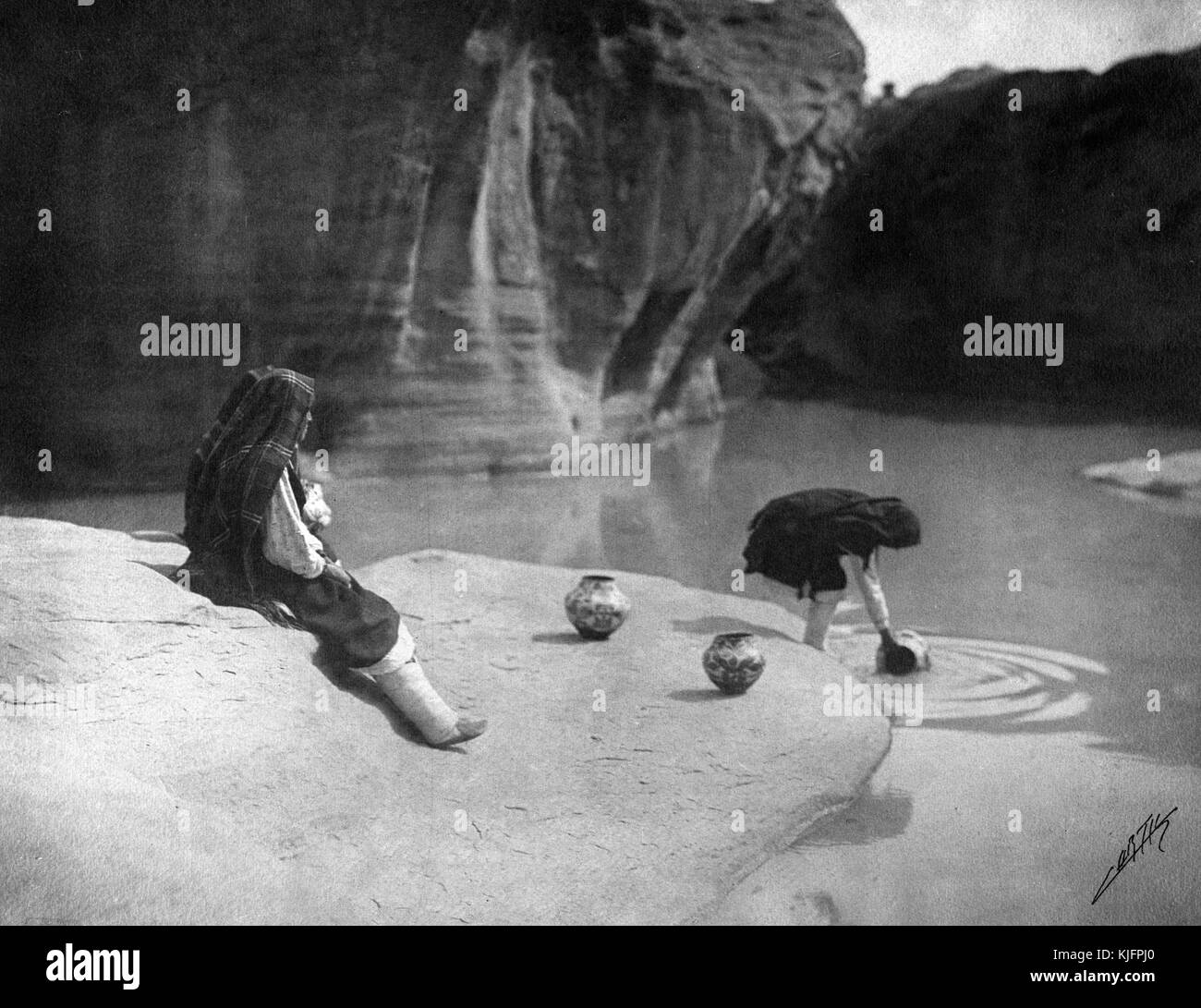 Foto von zwei indianischen Frauen, die Wasser in Tonkrügen an einem Brunnen sammeln, mit dem Titel „The Old Well of Acoma, Concept by many the malerischste Indian Village of the Southwest“, von Edward S Curtis, New Mexico, 1904. Aus der New York Public Library. Stockfoto