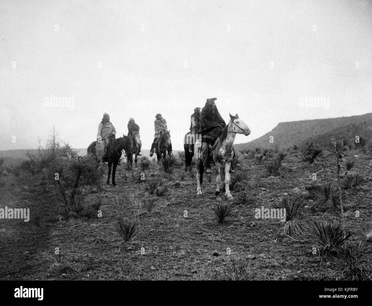 Foto mit vier indianischen Männern auf einem Pferderücken in einem Wüstengelände mit dem Titel „Desert Rovers (Apache)“ von Edward S Curtis, 1900. Aus der New York Public Library. Stockfoto