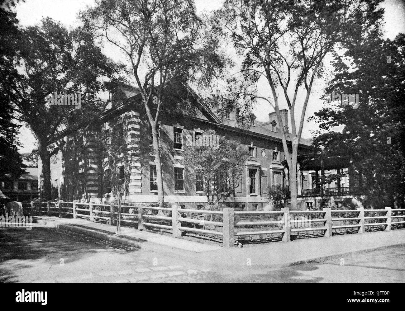 Ein Außenfoto der Harvard Union, es wurde 1900 gebaut, um einen Raum für Studenten, die nicht zu anderen Clubs in Harvard gehören, ein Zaun aus Steinsäulen und Holz Block von einem kleinen Hof mit Bäumen vor dem Gebäude, Es wurde erweitert und umgebaut, seit es gebaut wurde, schließlich wurde es umbenannt Barker Center, Cambridge, Massachusetts, Boston, Massachusetts, 1913. Stockfoto