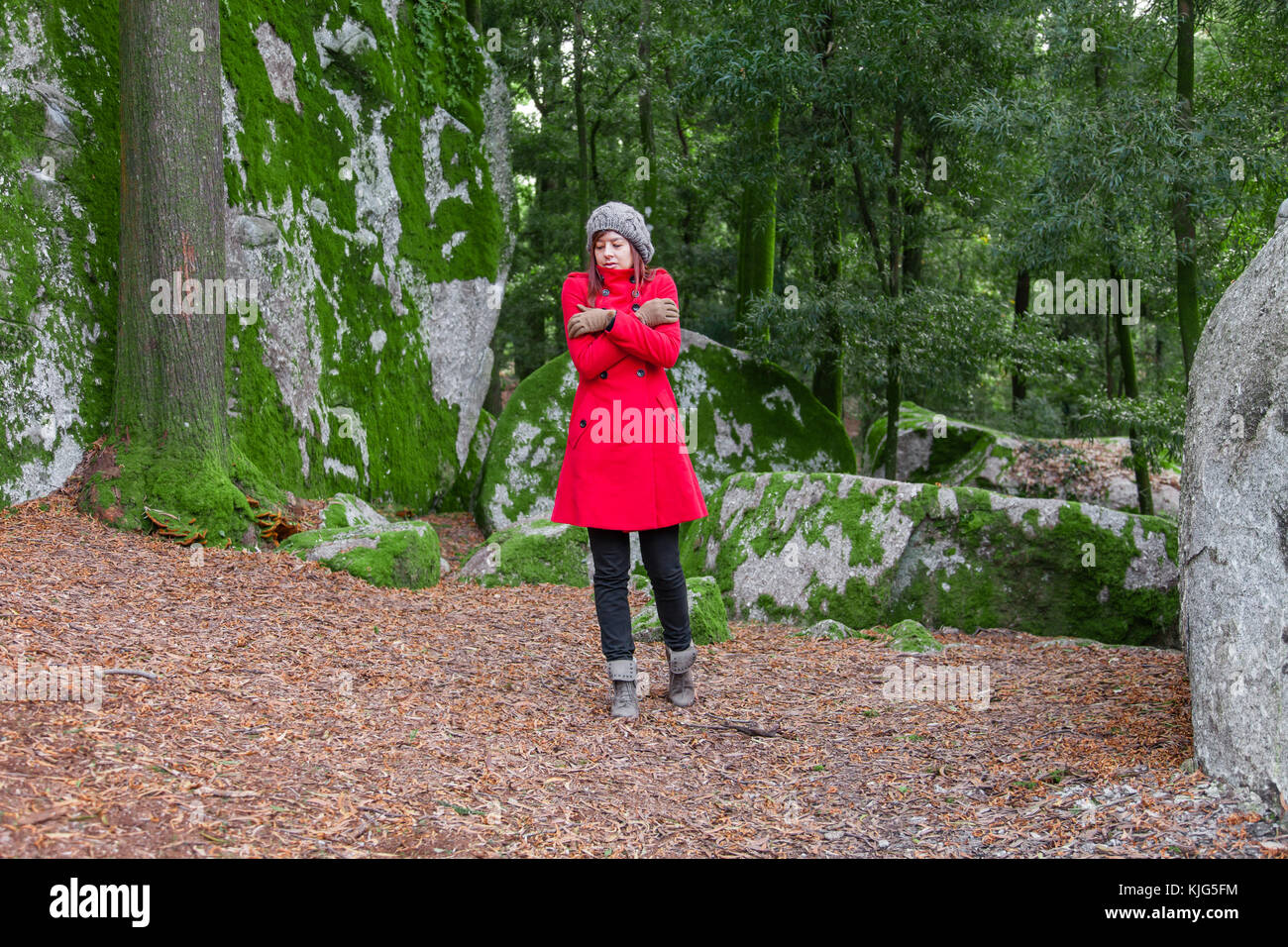 Junge Frau auf einem Wald zittern mit kalten und umarmen sich Holding verloren, trug einen roten Mantel oder Jacke, eine Mütze und Handschuhe während der Fal Stockfoto