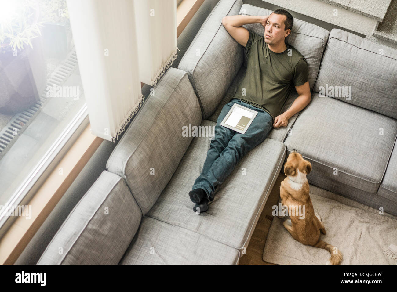 Mann zu Hause mit Tablet auf der Couch mit Hund neben ihm Stockfoto