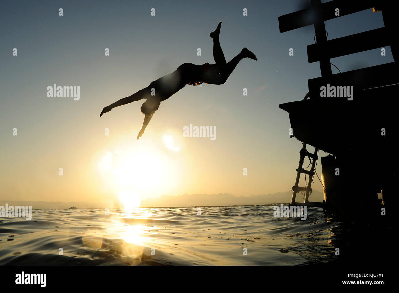 Mann springen fom Steg ins Meer bei Sonnenuntergang Stockfoto