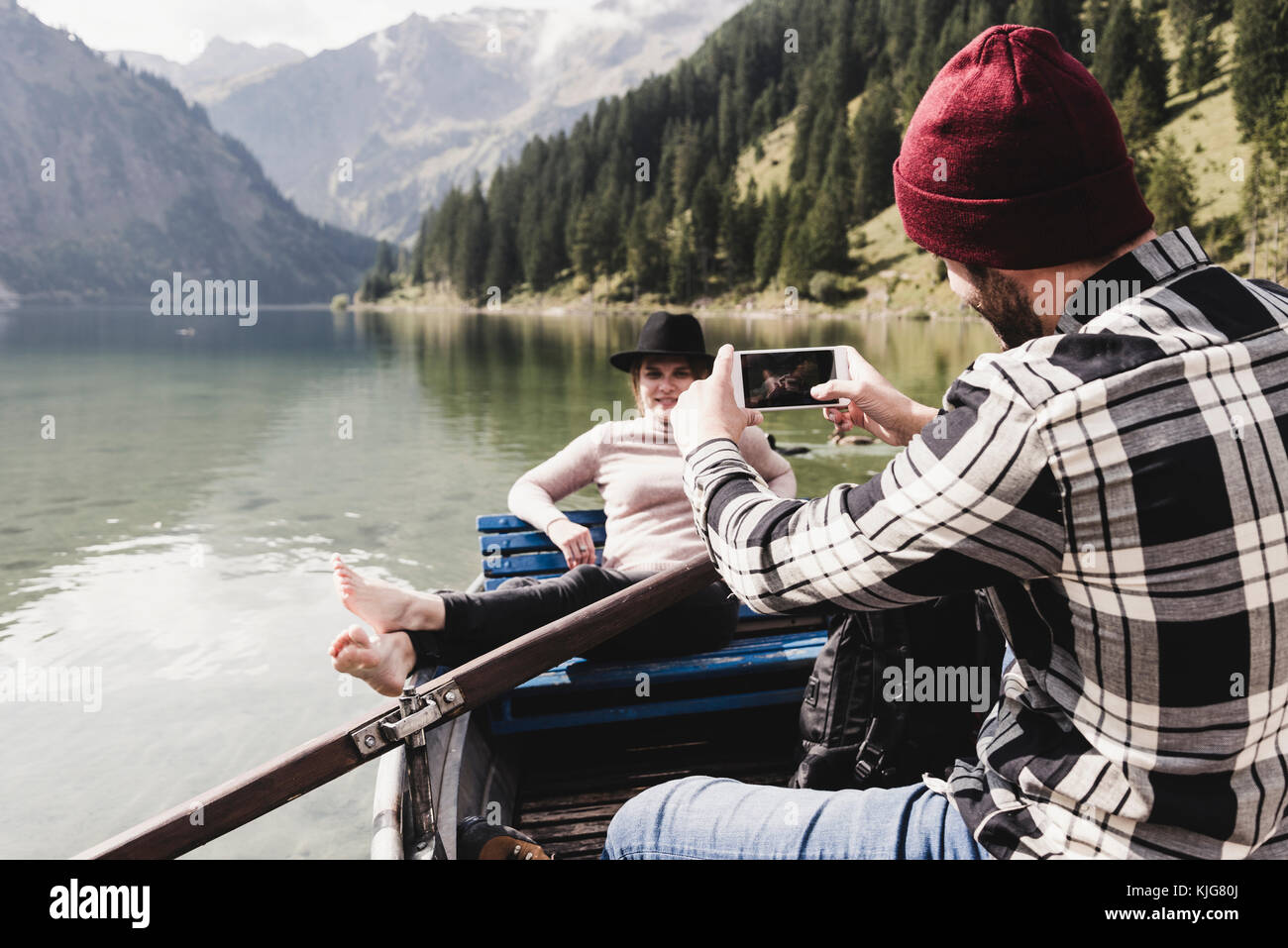 Österreich, Tirol, Alpen, Mann mit Handy Bild der Frau im Boot auf dem See Stockfoto