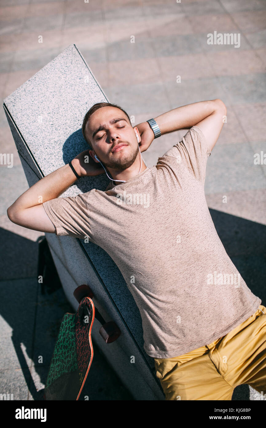 Junger Mann mit Ohrhörern und Longboard entspannen im Skatepark Stockfoto
