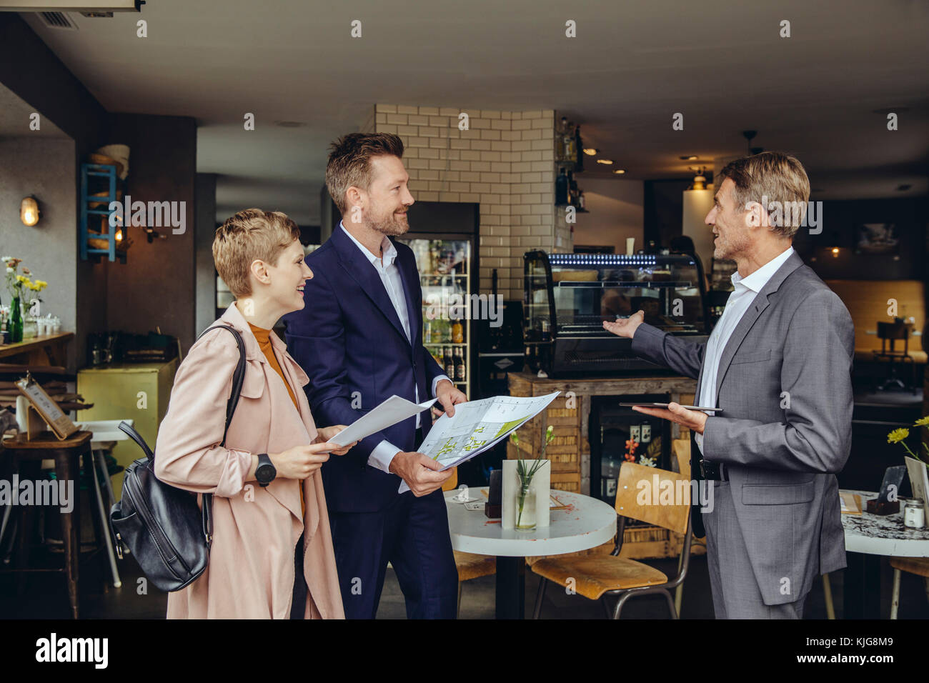 Frau und zwei Geschäftsleute über Pläne in einem Cafe Stockfoto