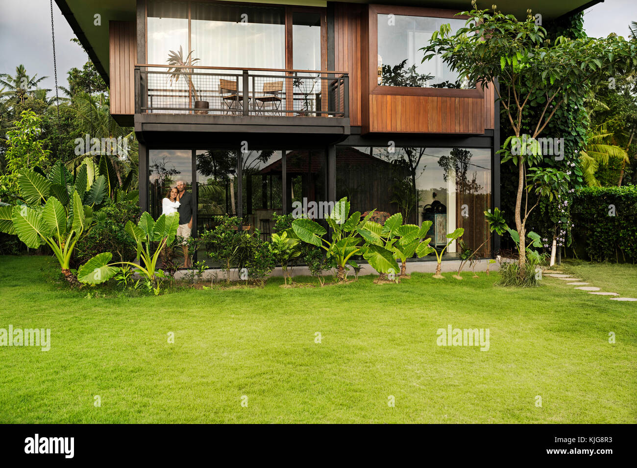 Garten Blick auf Paare stehen im modernen Design Haus umgeben von einem üppigen tropischen Garten Stockfoto