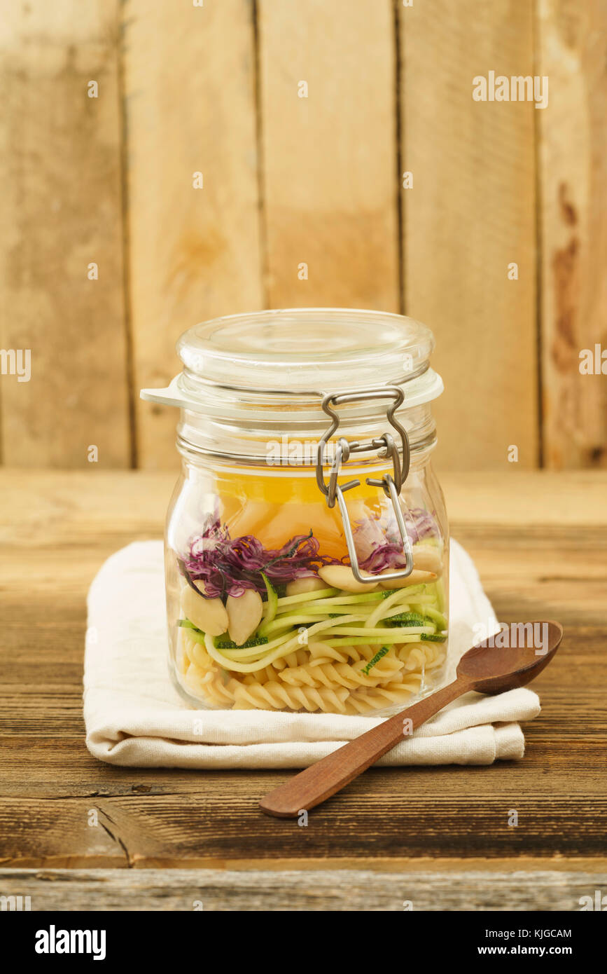 Veganer und vegetarischer Salat zum Mitnehmen im Glas mit Nudeln, spiralisierten Zucchini, Mandeln, Rotkohl und Vinaigrette in Holz Stockfoto