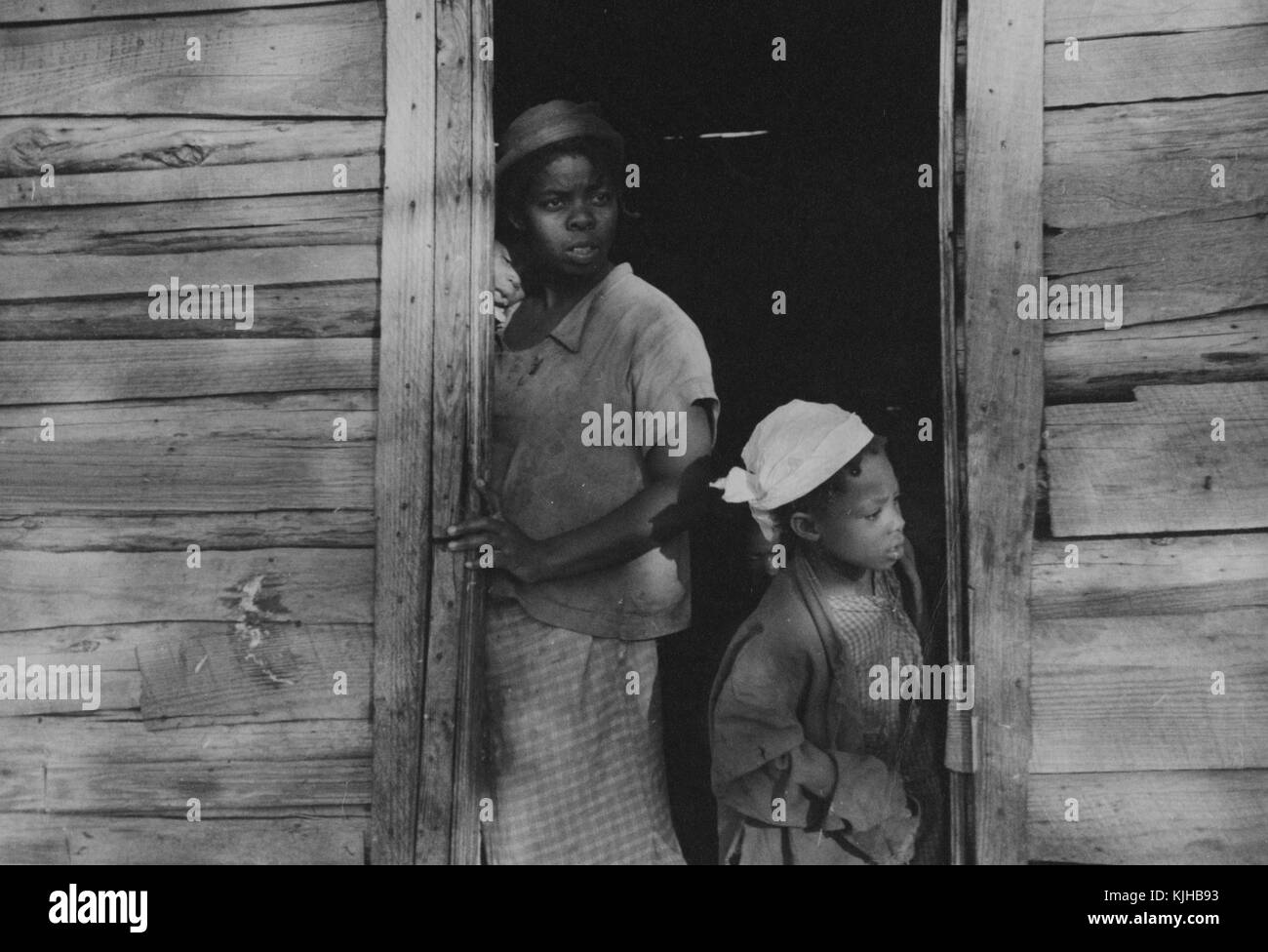 Ein Foto von einem Teenager Mädchen und einem jungen Mädchen in einer Tür, sie sind die Kinder einer Erdbeere, Bauer, beide sind auf der Suche nach etwas außerhalb des Bildes, sie sind beide tragen gemusterte Kleider mit leichte Jacken über, das Haus ist eine bescheidene hölzerne Struktur, Hammond, Louisiana, 1935. Von der New York Public Library. Stockfoto
