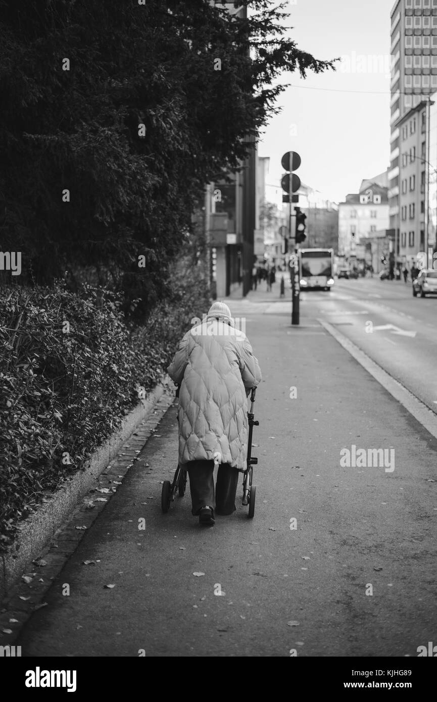 Ältere Frau zu Fuß durch den Bürgersteig mit einem Walker. Schwarz und Weiß. Stockfoto