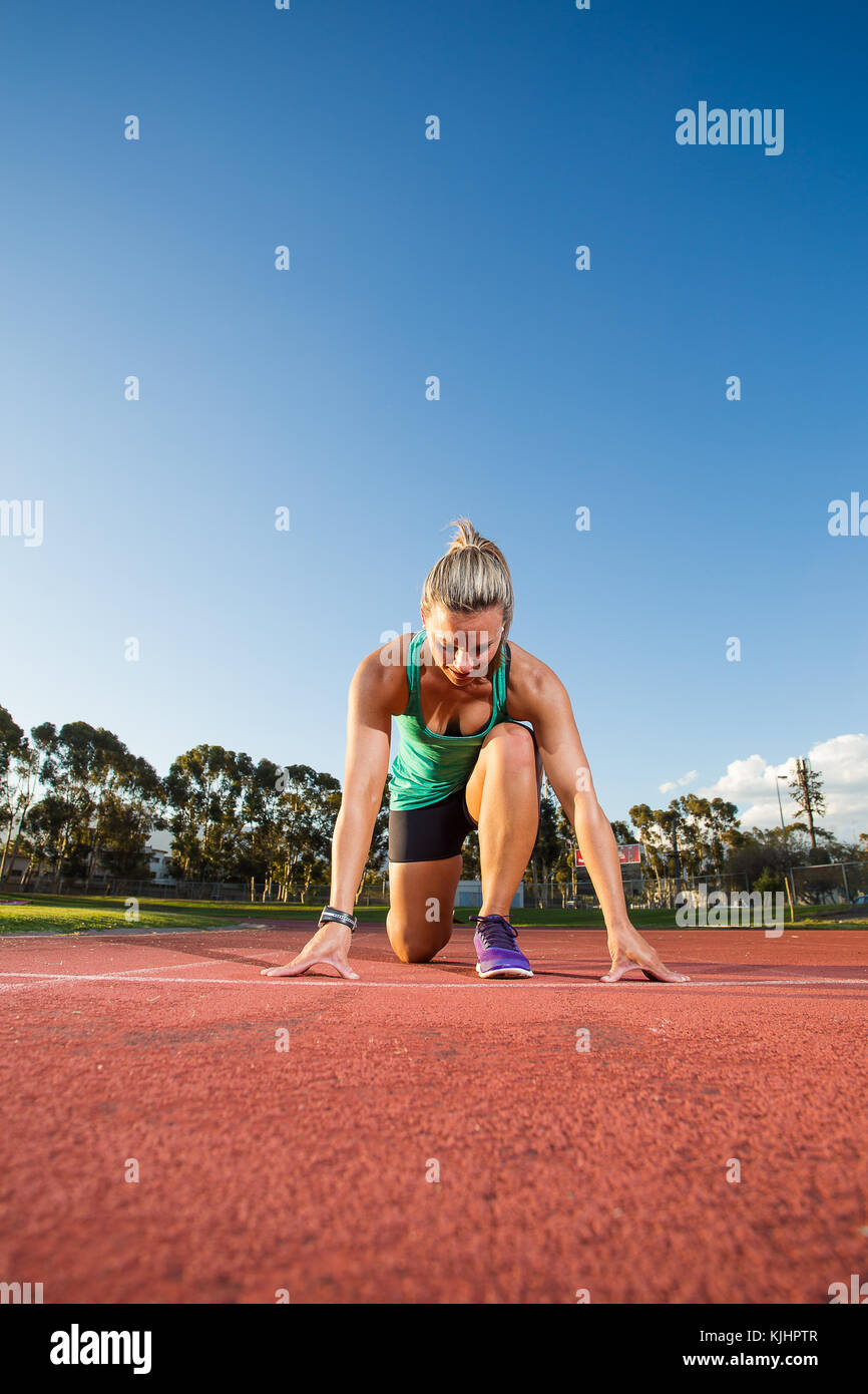 Nahaufnahme Weitwinkelaufnahme eines weiblichen sprinter Athlet fertig, ein Rennen auf einen tartan Rennstrecke mit dramatischen Beleuchtung am späten Nachmittag zu starten Stockfoto