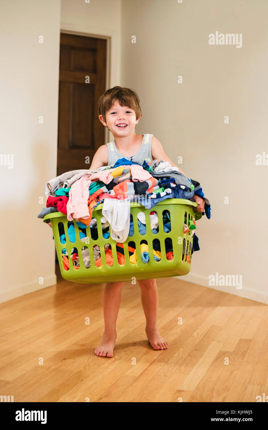 Lächelnde Junge Durchführung wäsche Korb gefüllt mit Kleidung Stockfoto