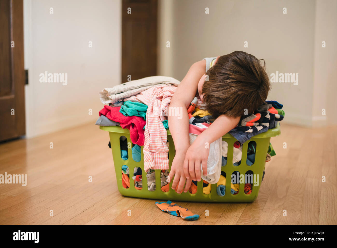 Junge Schlafen auf einer Wäsche Korb gefüllt mit Kleidung Stockfoto