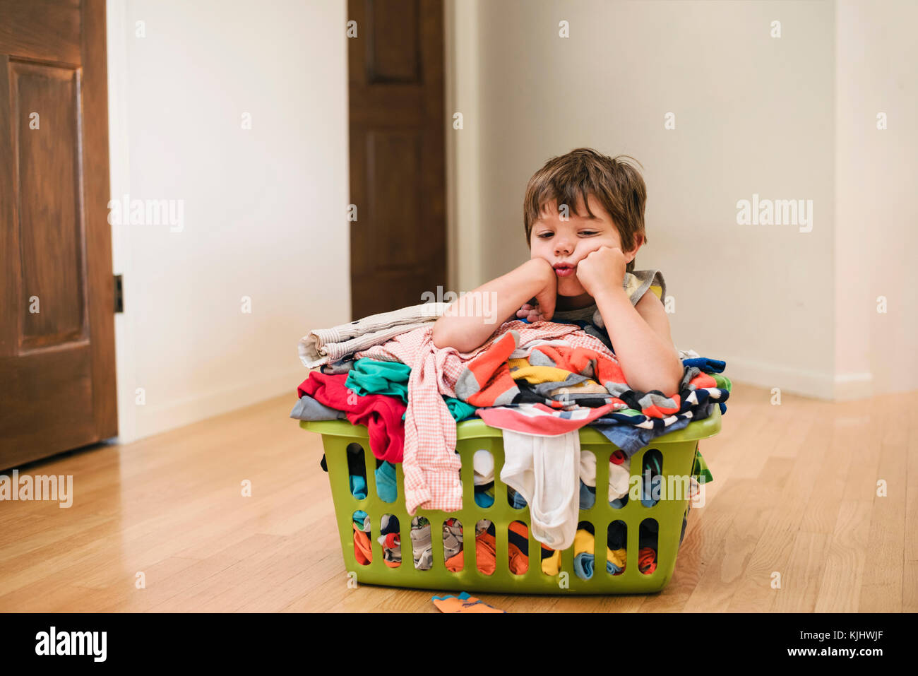 Müde Junge sitzt auf dem Boden lehnte sich auf der Wäsche Korb gefüllt mit Kleidung Stockfoto