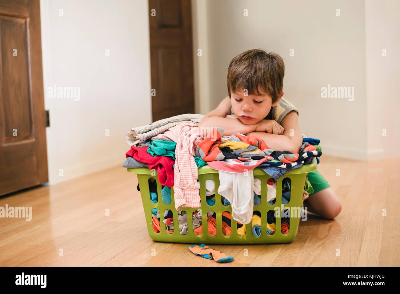 Müde Junge sitzt auf dem Boden lehnte sich auf der Wäsche Korb gefüllt mit Kleidung Stockfoto