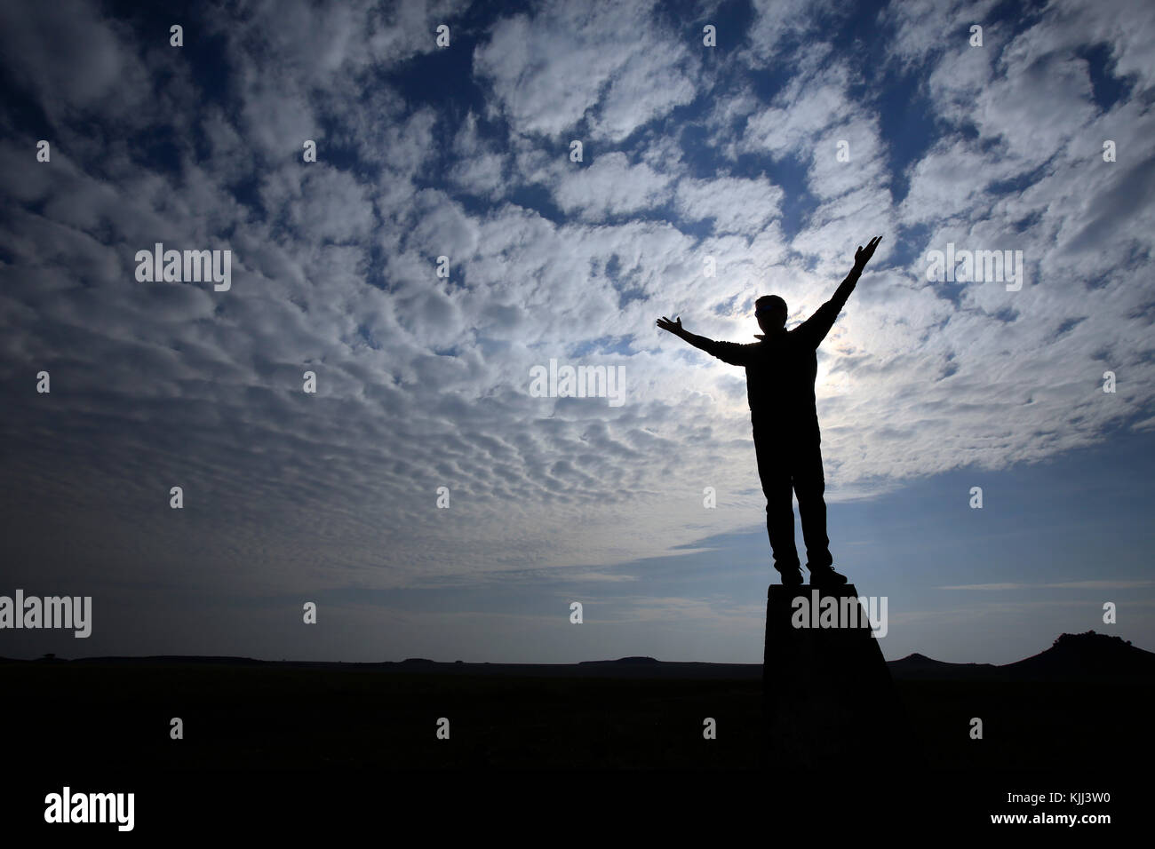 Mann mit erhobenen Armen beten gegen bewölkten Himmel. Silhouette. Stockfoto