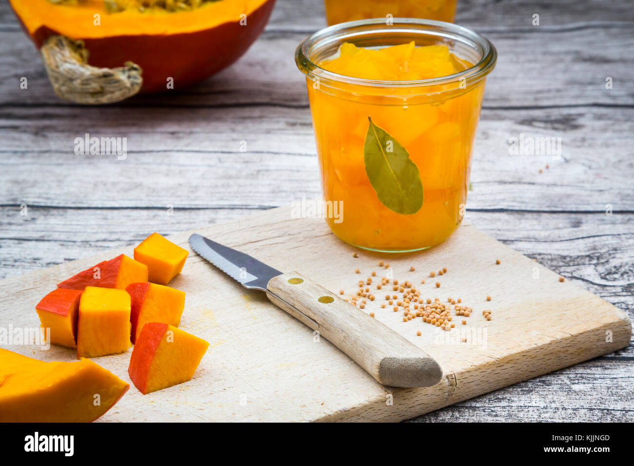 Glas süß-sauer eingelegten Kürbis, Senf Körner, Messer und gewürfelten Kürbis auf Holzbrett Stockfoto
