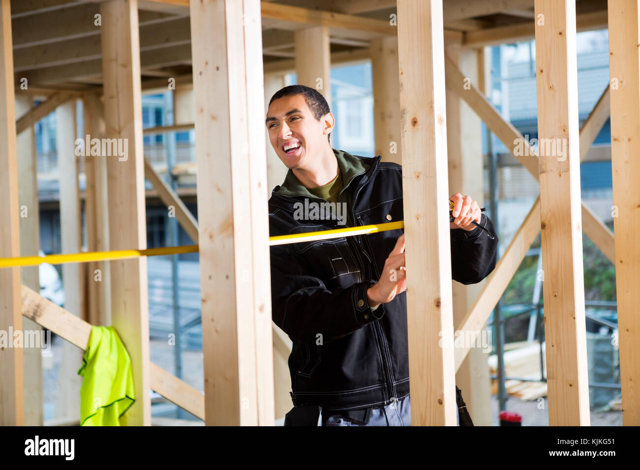 Junge männliche Tischler lachen während der Messung Holz auf der Baustelle Stockfoto