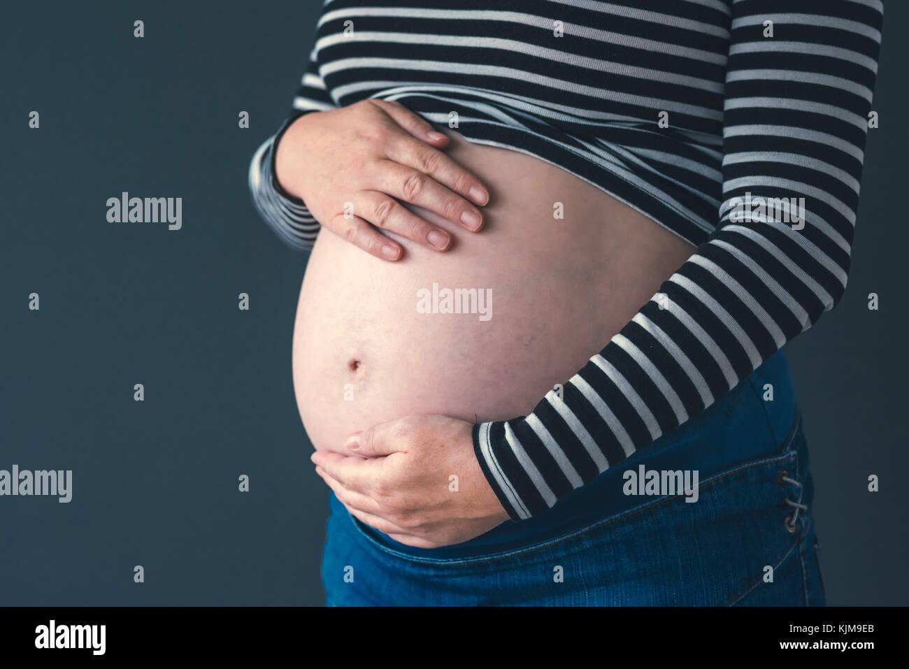 Freundliche, liebevolle Schwangere mit den Händen auf ihren Bauch im dritten Trimenon der Schwangerschaft erwarten neugeborenes Baby Stockfoto