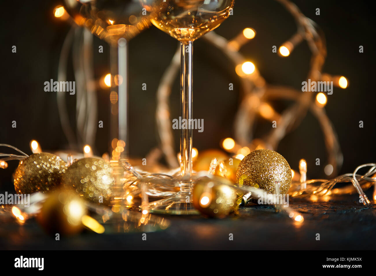 Zwei Gläser für Wein und goldene Weihnachtskugeln vor dem Hintergrund einer verschwommenen Golden Lights. geringe Tiefenschärfe. Stockfoto