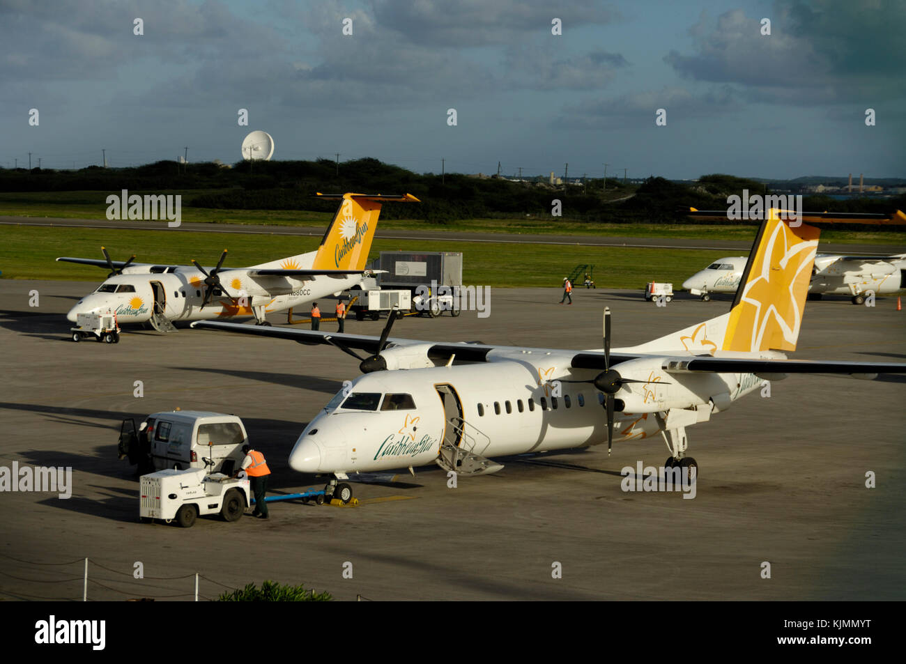Männer tragen gelbe High viz tabards zu Fuß zu einem Schlepper mit einer Anhängerzugvorrichtung, Caribbean Star Airlines Bombardier DHC-8 mit einer Caribbean Sun Airlines DHC-8 mit Stockfoto
