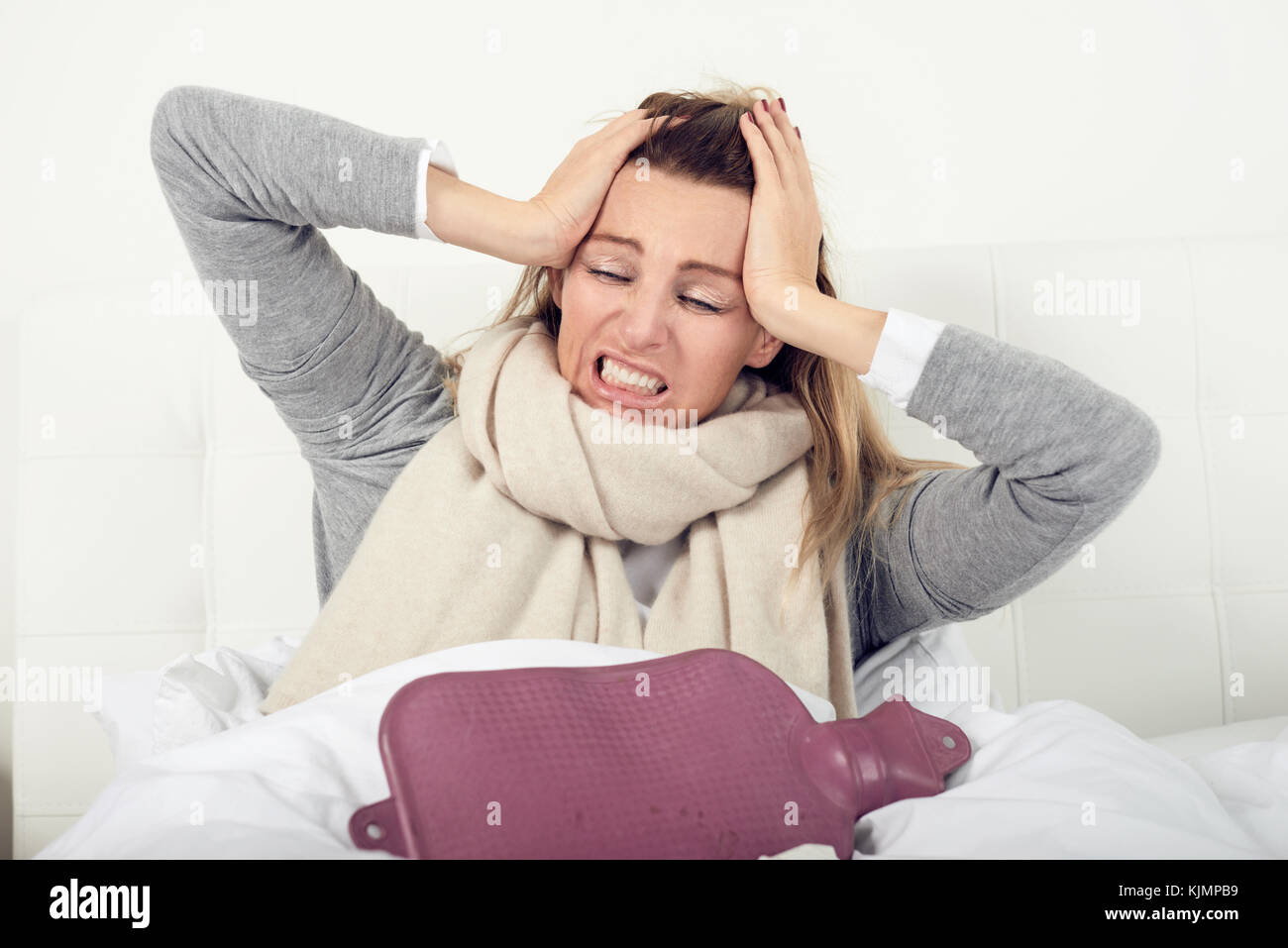 Porträt einer kranken Frau im Bett sitzend mit einer Wärmflasche beim Erfahren akute Kopfschmerzen durch Grippe oder andere schmerzhafte Krankheit verursacht Stockfoto