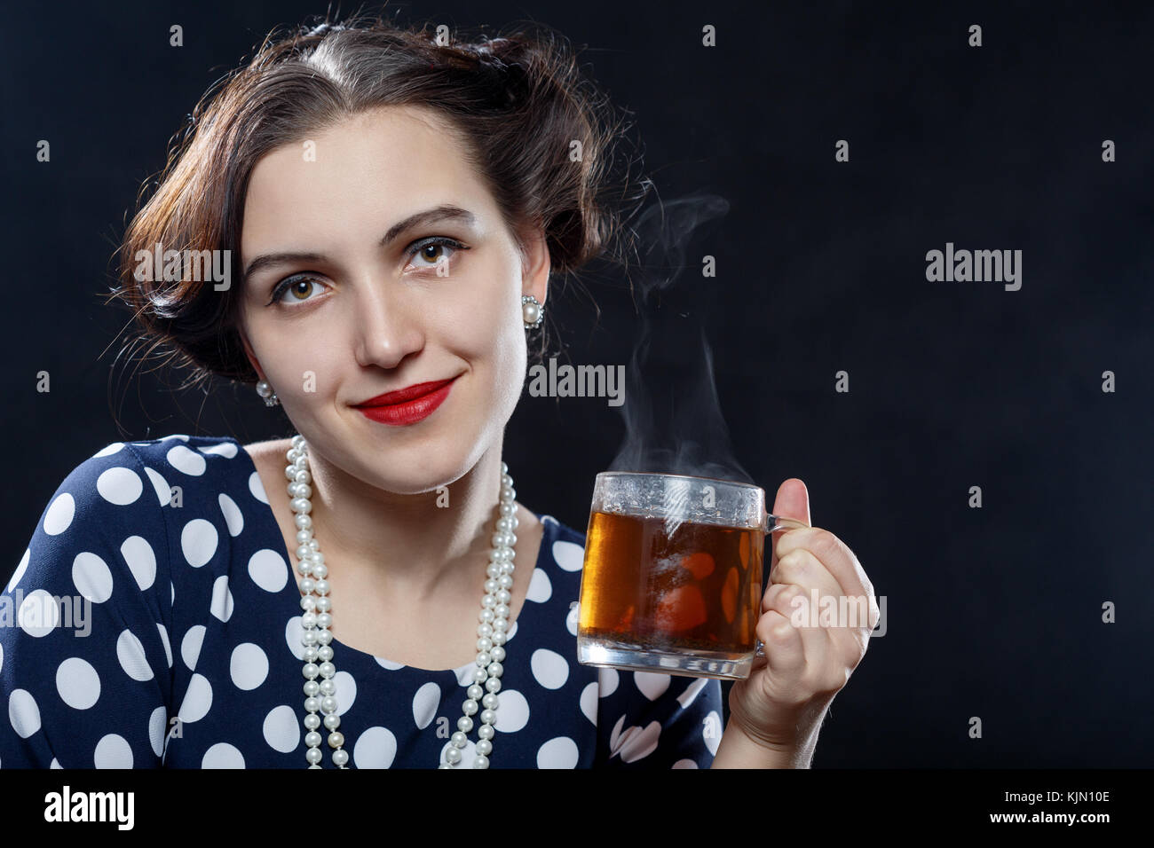 Schöne pinup Frau mit einer Tasse Tee auf schwarzem Hintergrund in die Kamera lächeln Stockfoto