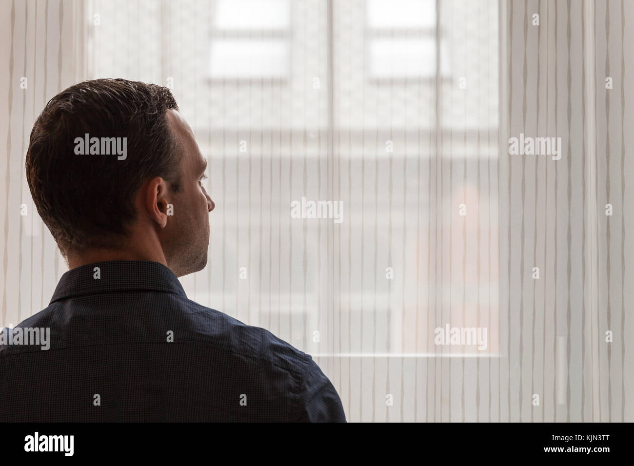 Junge Erwachsene europäische Mann steht in der Nähe von urbanen Fenster und sieht außerhalb, studio Foto mit selektiven Fokus Stockfoto