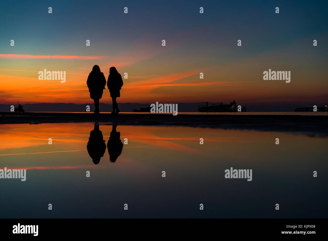 Reflexionen von zwei Womans Silhouetten zu Fuß durch das Meer, gegen Schöne nach Sonnenuntergang Farbtöne Stockfoto