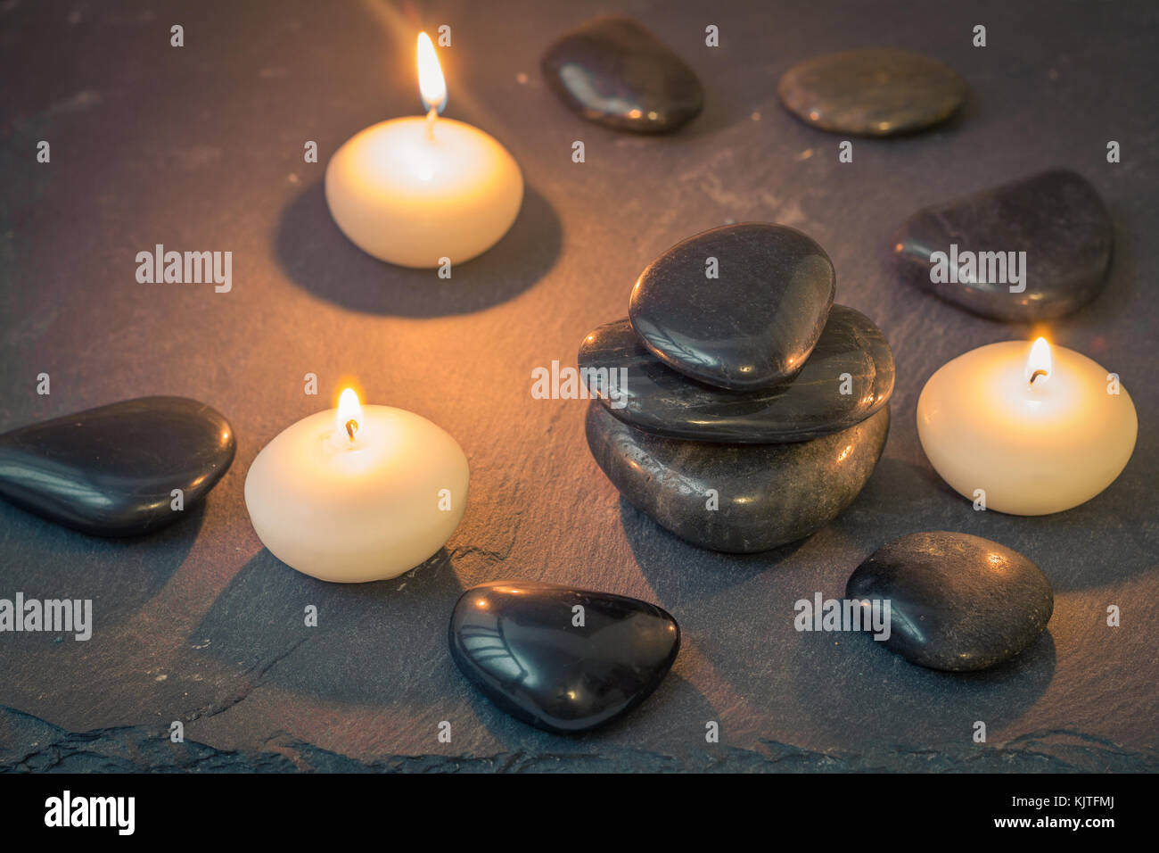 Schwarze Steine und brennende Kerzen auf dunklem Hintergrund Stockfoto