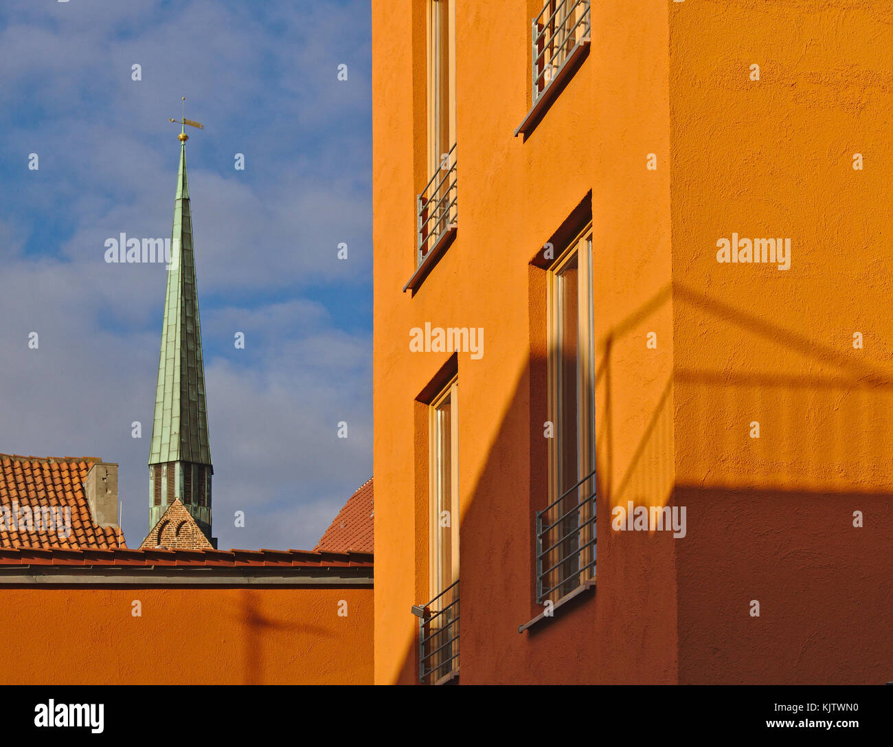 Helles orange Fassade der modernen Wohngebäude beleuchtet durch die Abendsonne mit Kirchturm im Hintergrund Stockfoto