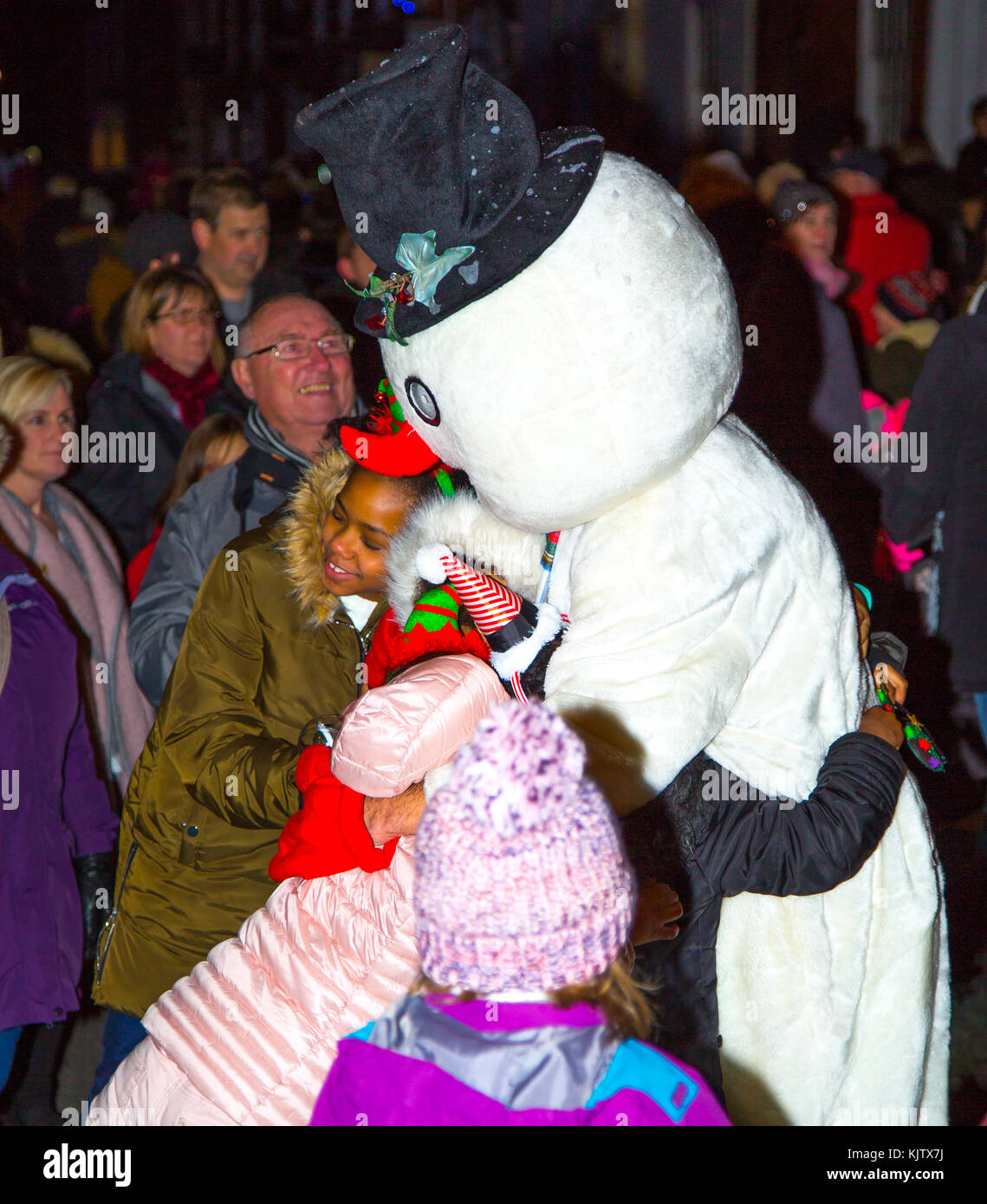 Aufgeregte Kinder eilen, während einer britischen Weihnachtstraßenparade enorme Umarmungen von Frosty the Snowman zu erhalten. Ein magischer Moment. Stockfoto