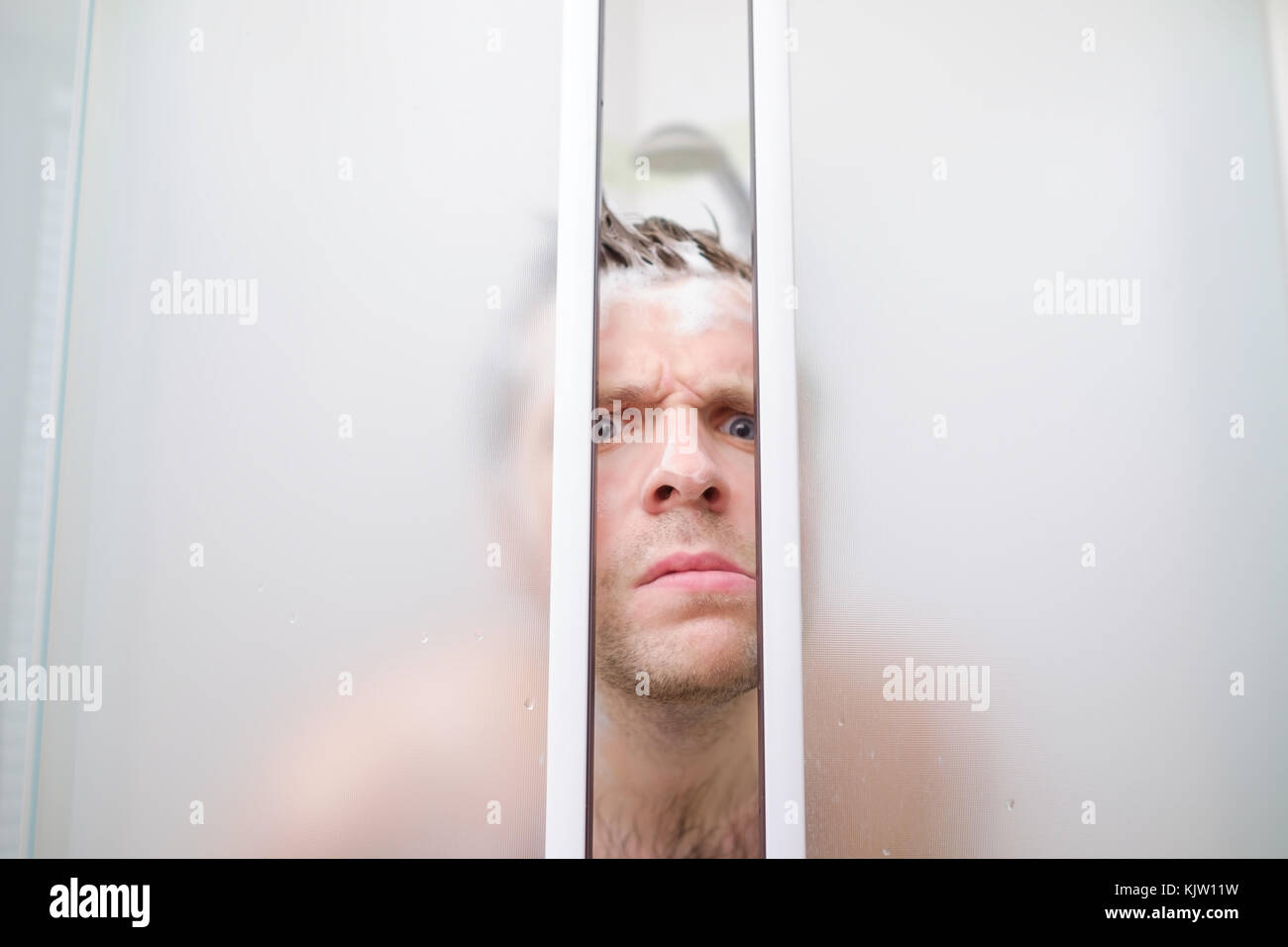 Ein junger kaukasischer Mann guckt aus der Dusche in der Seife. Stockfoto