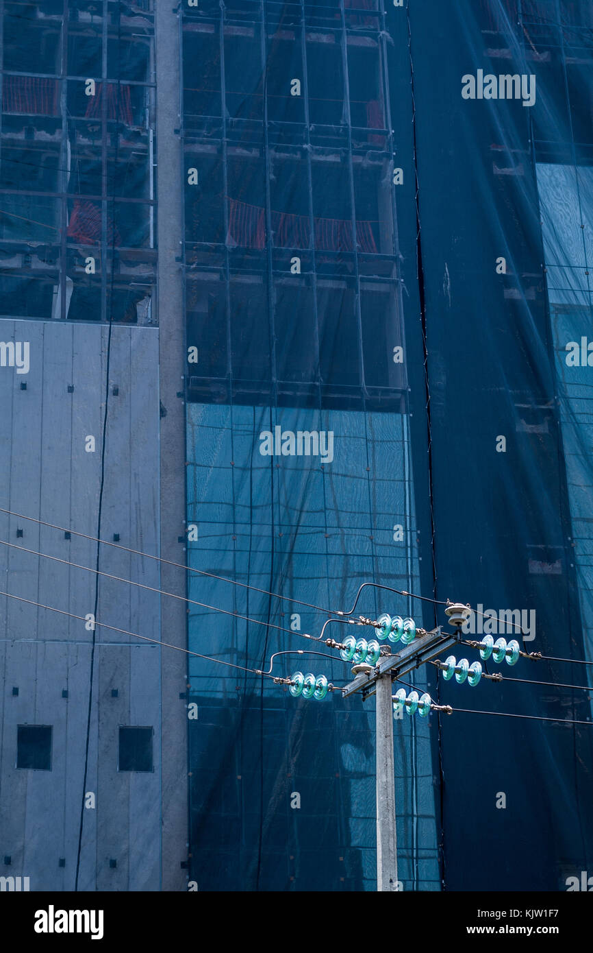 Hohe Spannung Lichtmast mit einem Gebäude im Bau als Hintergrund bedeckt mit einer Leinwand, das Blau des Himmels spiegelt. Stockfoto