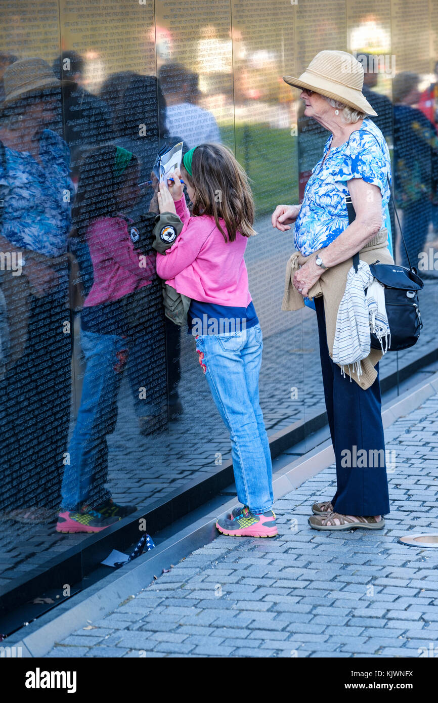 Junge Mädchen Kopieren der Name eines Soldaten, relative, während sie von einer älteren Frau an der Vietnam Veterans Memorial, Washington, D.C., USA beobachtet werden. Stockfoto