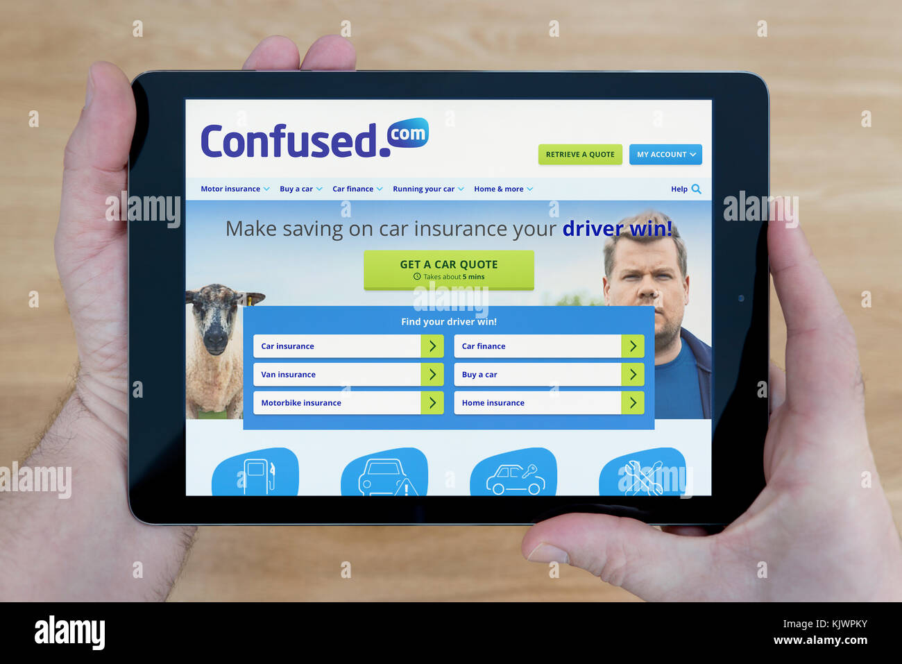 Ein Mann schaut auf die confused.com Website auf seinem iPad tablet device, Schuß gegen einen hölzernen Tisch top Hintergrund (nur redaktionelle Nutzung) Stockfoto