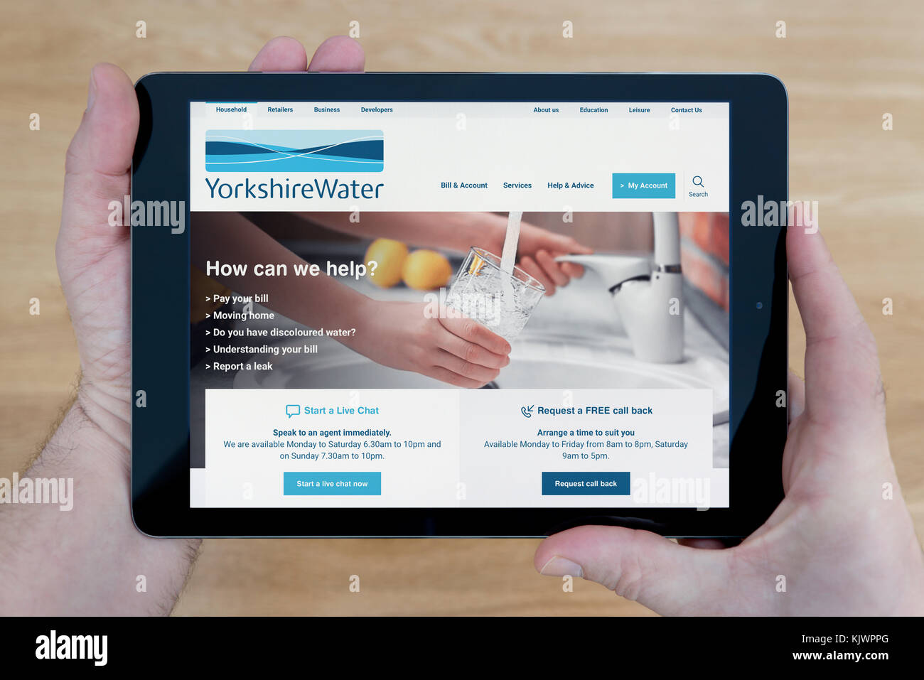 Ein Mann schaut auf die Yorkshire Water Website auf seinem iPad tablet device, Schuß gegen einen hölzernen Tisch top Hintergrund (nur redaktionelle Nutzung) Stockfoto