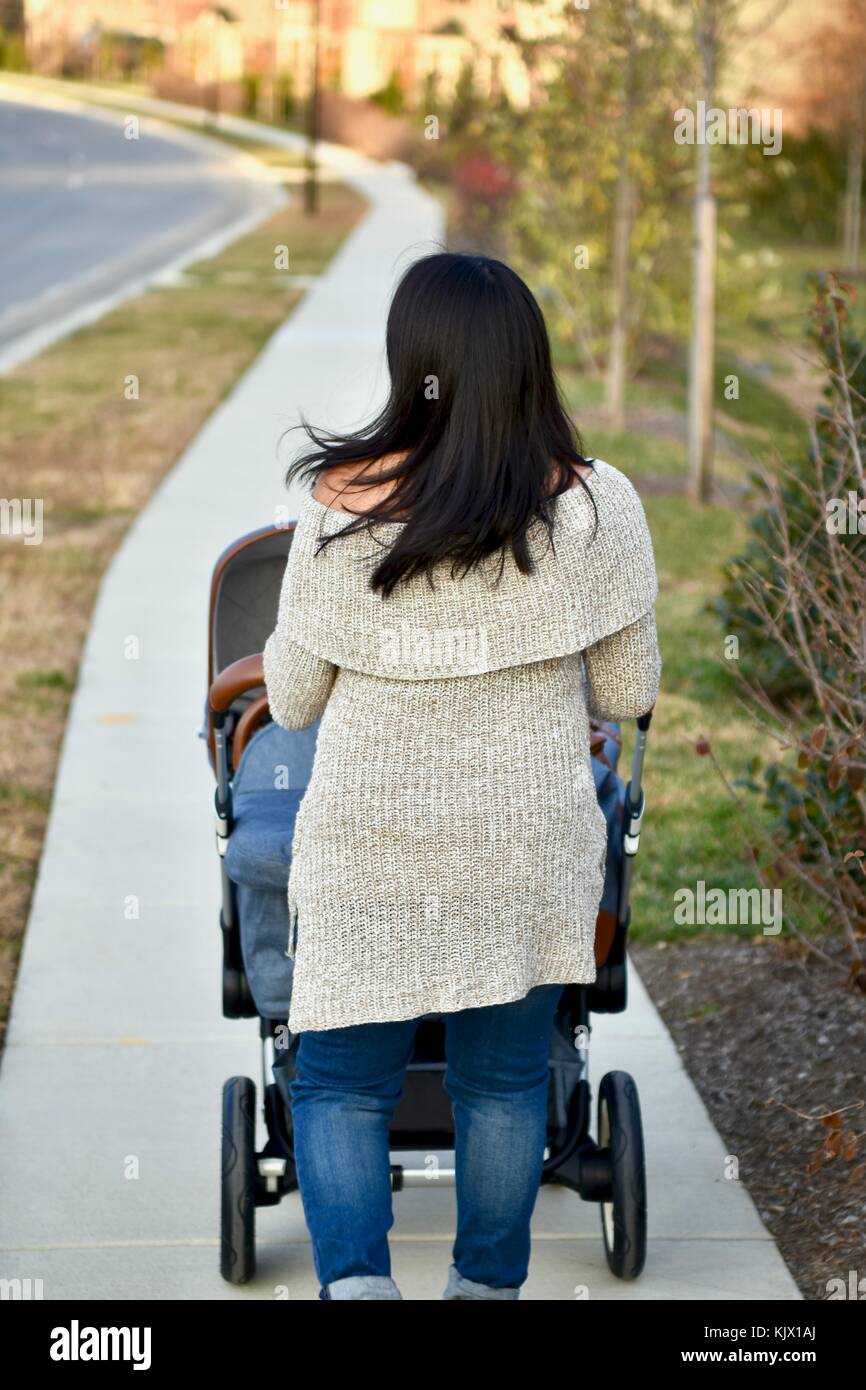 Frau, die den Bugaboo Kinderwagen auf den Bürgersteig drückt Stockfoto