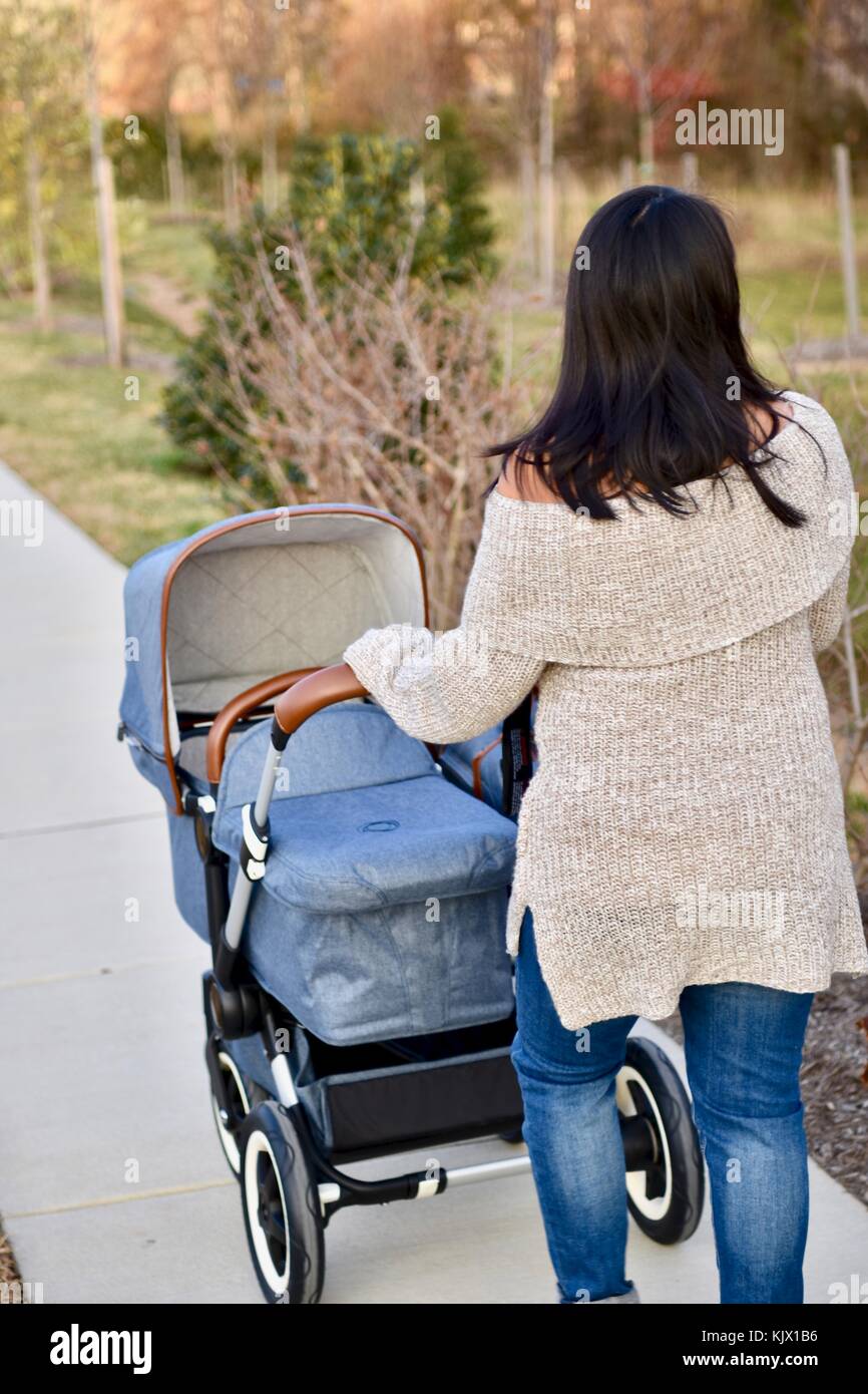 Frau, die den Bugaboo Kinderwagen auf den Bürgersteig drückt Stockfoto