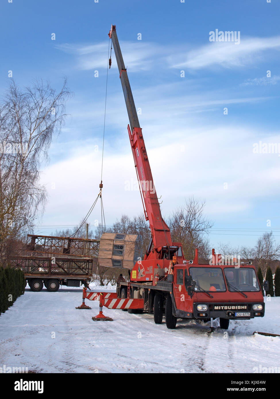 NICA, LETTLAND - 20. FEBRUAR 2013: Schwere Mobilkran heben Metallturmteile zum Verladen auf LKW-Anhänger bei schneebedecktem Wintersonnenuntergang an. Stockfoto