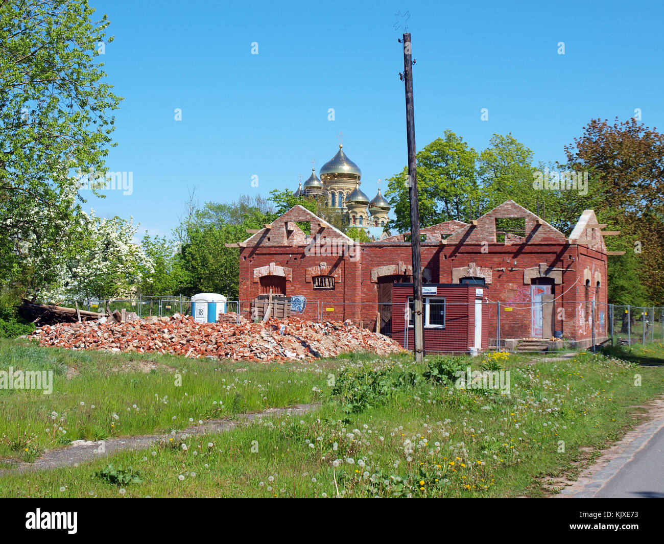 LIEPAJA, LETTLAND - 21. MAI 2015: Hinter den Ruinen des roten Backsteinhauses sind goldene Kuppeln der Kathedrale zu sehen. Stockfoto