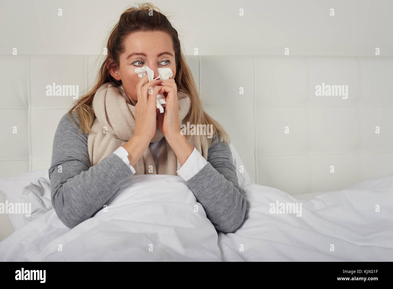 Kranke Frau mit saisonalen Kälte und Grippe liegen, gemütlich im Bett mit einem miserablen Ausdruck ihrer Nase Blasen auf einem Gewebe umwickelt Stockfoto